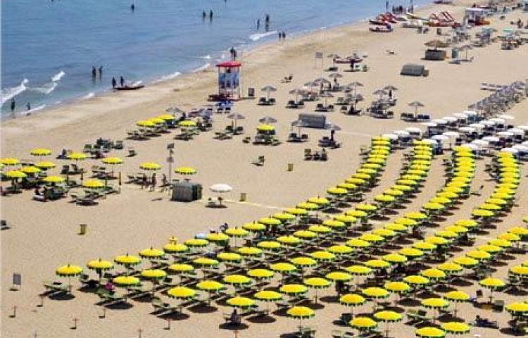 Spiaggia estiva affollata, ombrelloni gialli, mare blu, sole, gioia e relax.